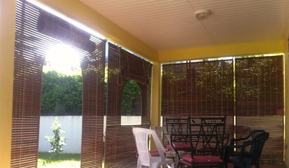 Varangue aux murs jaunes fermée par des stores, avec un passage en arche par où entre le soleil