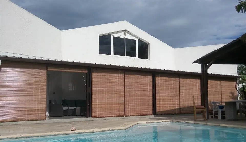 Grande varangue fermée par des stores mauriciens au bord d'une piscine
